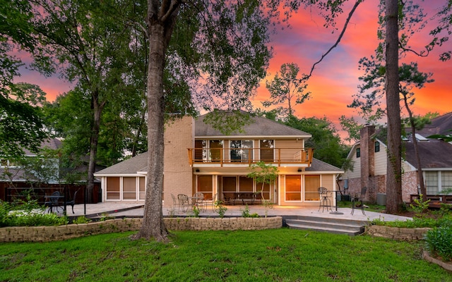 back house at dusk with a lawn, a balcony, and a patio