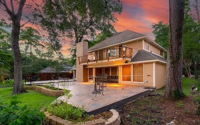 back house at dusk with a yard, a balcony, and a patio