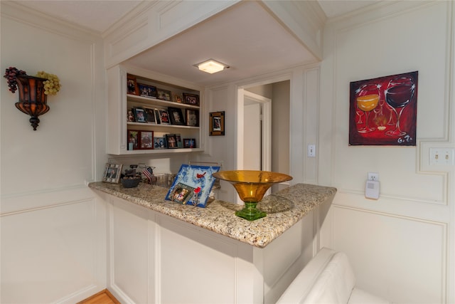 kitchen with light stone countertops, built in features, and ornamental molding