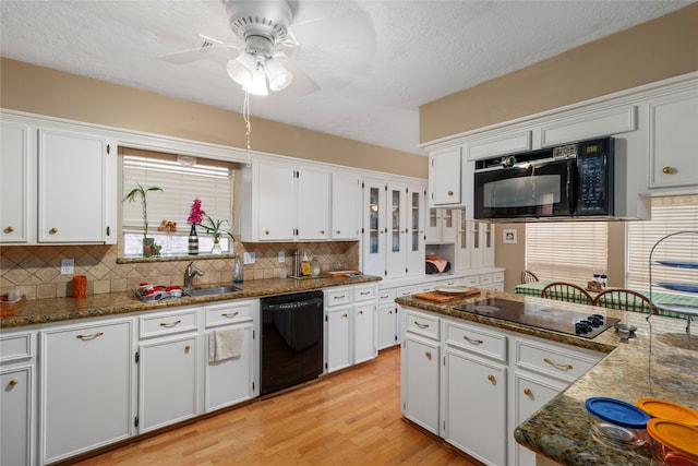 kitchen with plenty of natural light, white cabinets, black appliances, and light hardwood / wood-style floors