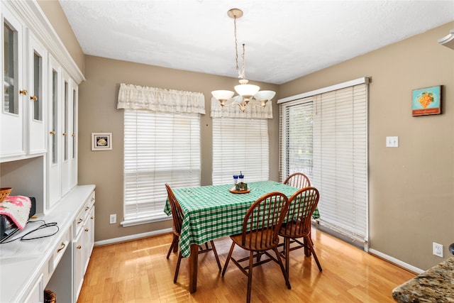 dining area with a textured ceiling, light hardwood / wood-style floors, an inviting chandelier, and plenty of natural light