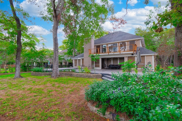 rear view of house featuring a balcony, a garage, and a lawn