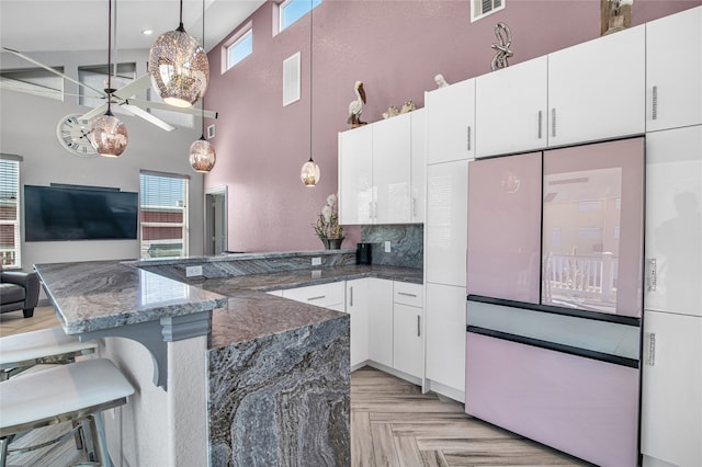 kitchen with a kitchen breakfast bar, a wealth of natural light, white cabinets, a high ceiling, and hanging light fixtures