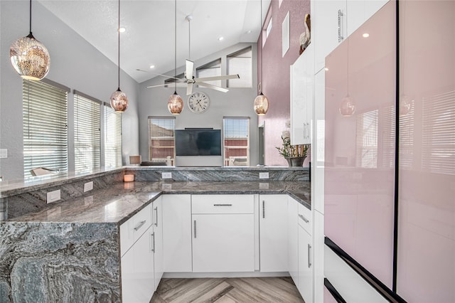 kitchen with dark stone counters, ceiling fan, pendant lighting, high vaulted ceiling, and white cabinetry