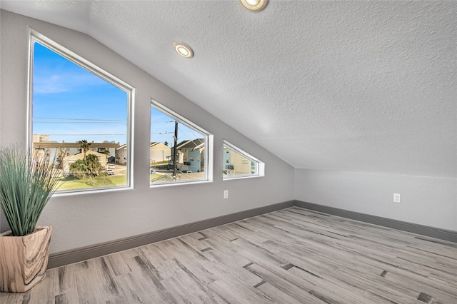 additional living space with lofted ceiling, a textured ceiling, and light hardwood / wood-style flooring