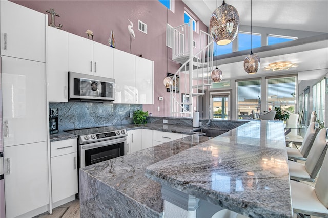 kitchen with pendant lighting, dark stone counters, vaulted ceiling, white cabinetry, and stainless steel appliances