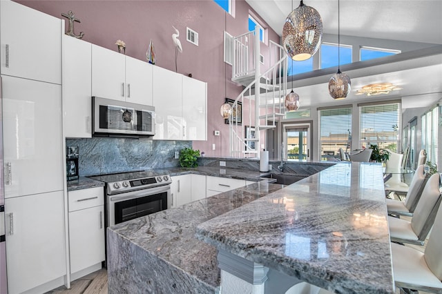 3709 Rice St, Galveston, TX 77554 - kitchen with a kitchen breakfast bar, white cabinetry, a peninsula, tasteful backsplash, and hanging light fixtures