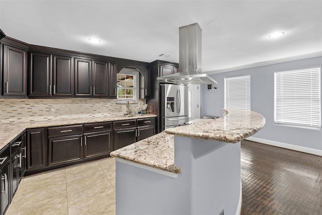 kitchen featuring a center island, stainless steel fridge, tasteful backsplash, light stone counters, and island exhaust hood