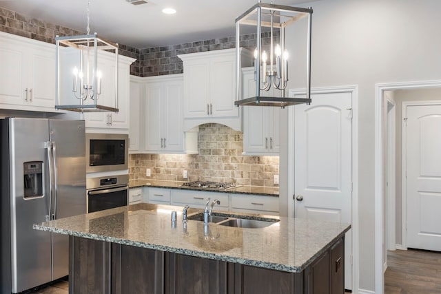 kitchen with a kitchen island with sink, sink, stainless steel appliances, and dark stone counters