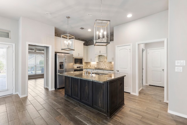 kitchen featuring dark stone counters, a center island with sink, sink, dark hardwood / wood-style floors, and appliances with stainless steel finishes