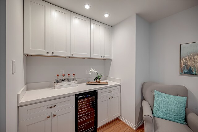 bar with white cabinets, beverage cooler, and light wood-type flooring