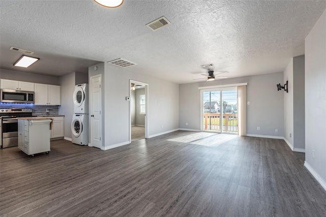 interior space with ceiling fan, dark hardwood / wood-style flooring, a textured ceiling, and stacked washer and clothes dryer