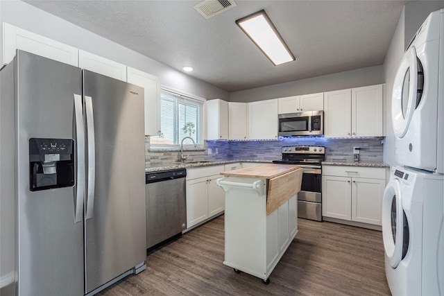 kitchen featuring white cabinets, sink, appliances with stainless steel finishes, light stone counters, and stacked washer / dryer