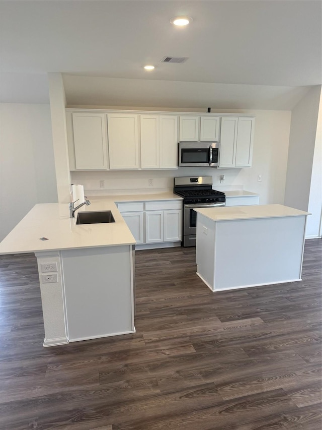 kitchen featuring kitchen peninsula, stainless steel appliances, dark wood-type flooring, sink, and white cabinets