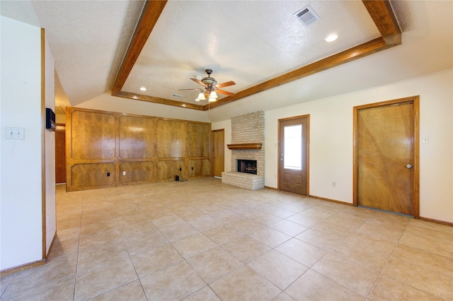 unfurnished living room featuring a raised ceiling, ceiling fan, a fireplace, a textured ceiling, and light tile patterned flooring