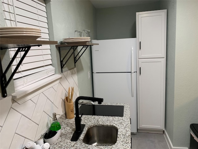 kitchen with light stone counters, sink, white cabinets, and white refrigerator