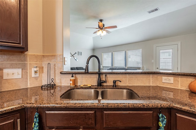 kitchen with dark brown cabinetry, ceiling fan, sink, and dark stone countertops