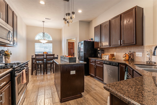 kitchen with sink, stainless steel appliances, hanging light fixtures, light hardwood / wood-style floors, and a kitchen island