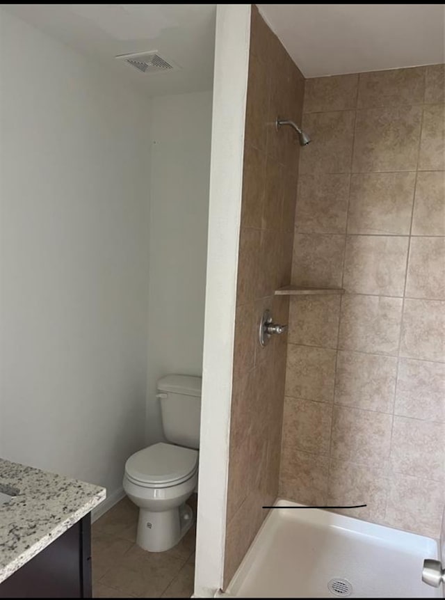 bathroom featuring tile patterned flooring, a tile shower, vanity, and toilet