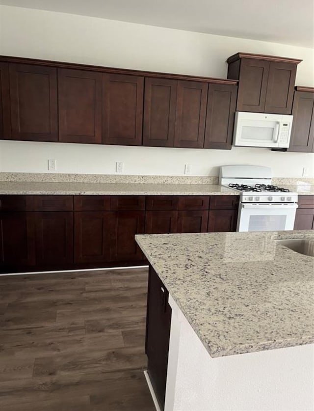 kitchen featuring dark brown cabinets, white appliances, light stone counters, and dark wood-type flooring