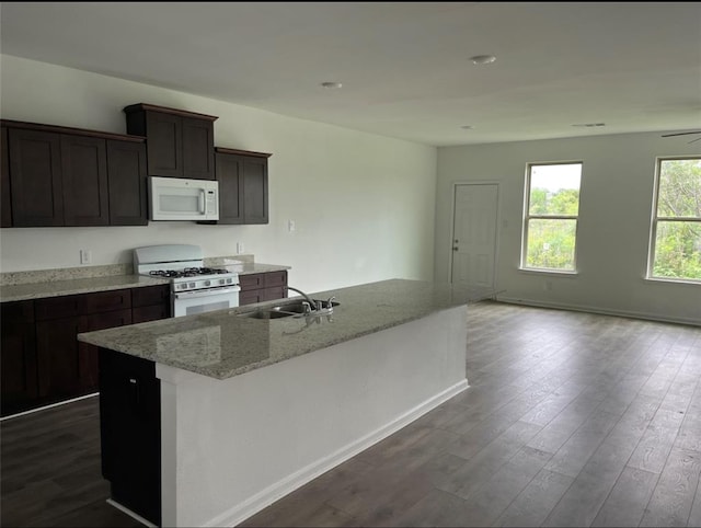 kitchen with white appliances, a kitchen island with sink, sink, dark hardwood / wood-style floors, and light stone counters