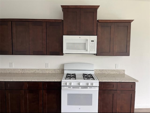 kitchen featuring light stone countertops, dark brown cabinets, white appliances, and hardwood / wood-style flooring