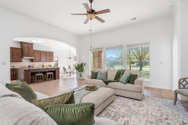 tiled living room with ceiling fan with notable chandelier and ornamental molding