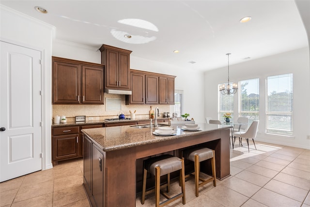 kitchen featuring sink, tasteful backsplash, crown molding, a chandelier, and a center island with sink