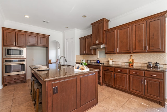 kitchen featuring backsplash, stainless steel appliances, crown molding, sink, and an island with sink