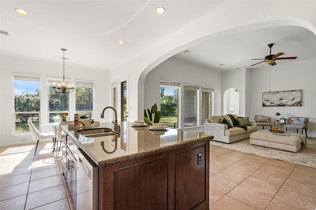 kitchen with light stone countertops, ceiling fan with notable chandelier, a kitchen island with sink, light tile patterned floors, and decorative light fixtures