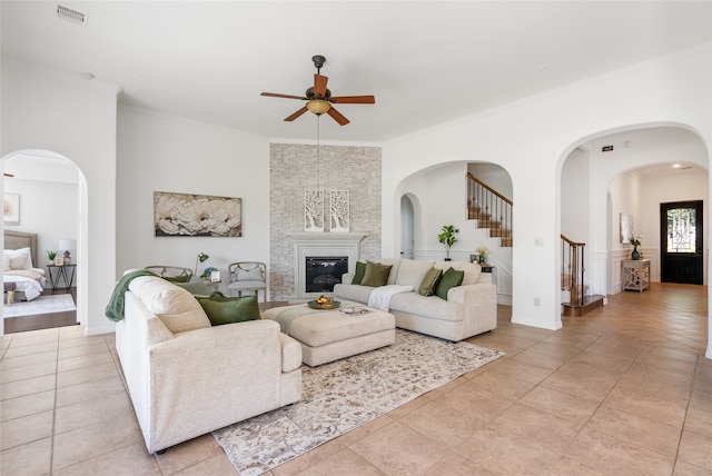 tiled living room featuring ceiling fan, a large fireplace, and ornamental molding