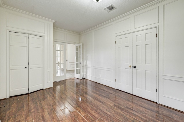 unfurnished bedroom featuring french doors, a textured ceiling, dark hardwood / wood-style floors, and crown molding