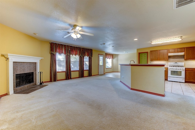 unfurnished living room featuring a textured ceiling, ceiling fan, light colored carpet, and a fireplace