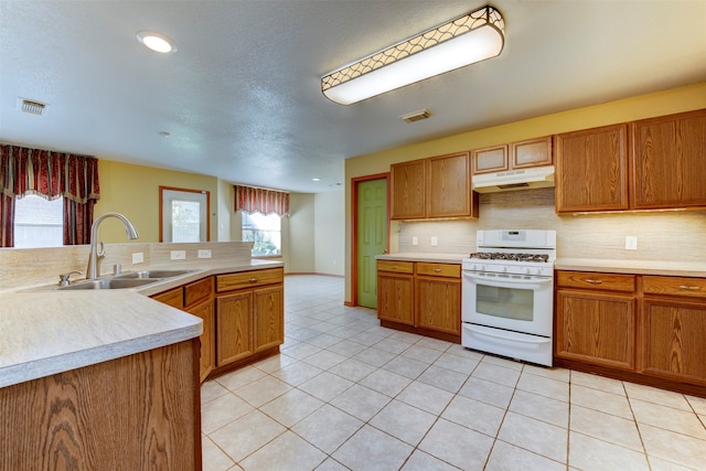 kitchen with backsplash, white gas range, sink, and light tile patterned floors