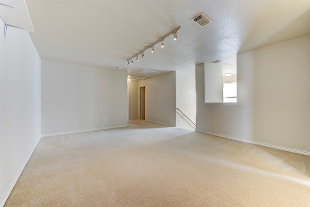 empty room with a textured ceiling, rail lighting, and light colored carpet