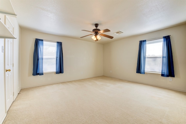 carpeted spare room with a textured ceiling, plenty of natural light, and ceiling fan