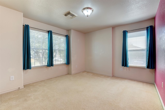 empty room with a healthy amount of sunlight, a textured ceiling, and light carpet