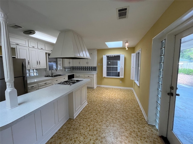 kitchen featuring decorative backsplash, appliances with stainless steel finishes, a skylight, sink, and white cabinetry