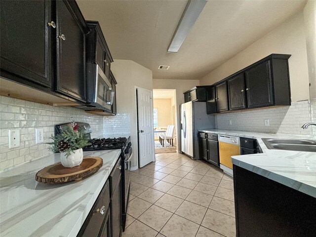 kitchen with sink, decorative backsplash, light stone countertops, appliances with stainless steel finishes, and light tile patterned flooring