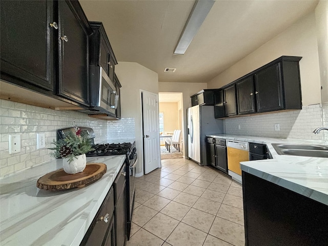 kitchen with light tile patterned flooring, sink, stainless steel appliances, light stone countertops, and decorative backsplash