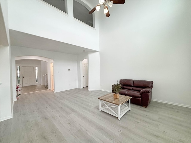 living room with a towering ceiling, light hardwood / wood-style flooring, and ceiling fan