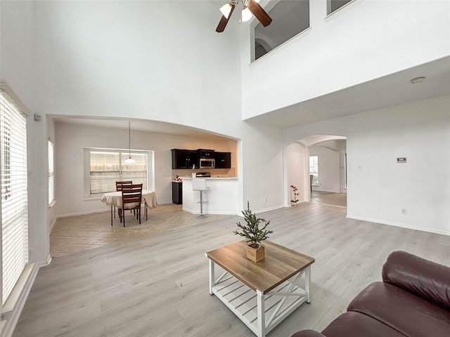 living room featuring a towering ceiling, ceiling fan, and light hardwood / wood-style flooring