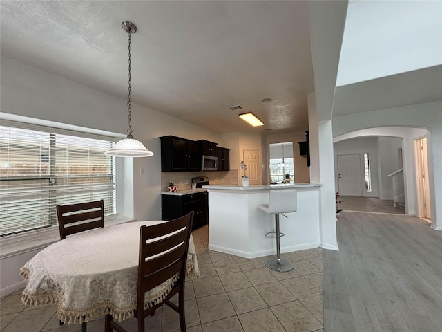 kitchen with pendant lighting, backsplash, a kitchen breakfast bar, kitchen peninsula, and stainless steel appliances