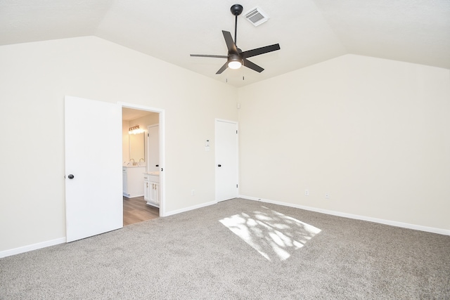 unfurnished bedroom featuring dark carpet, ensuite bath, vaulted ceiling, and ceiling fan