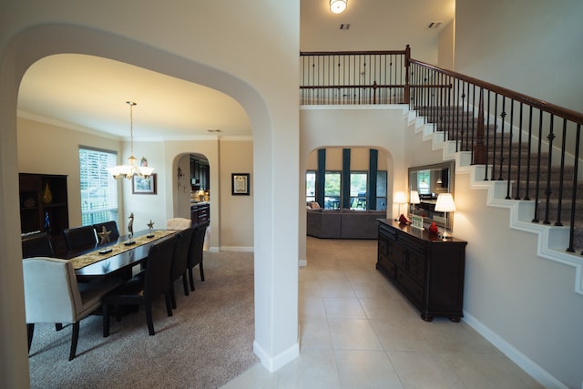 dining space with a towering ceiling, light colored carpet, an inviting chandelier, and crown molding