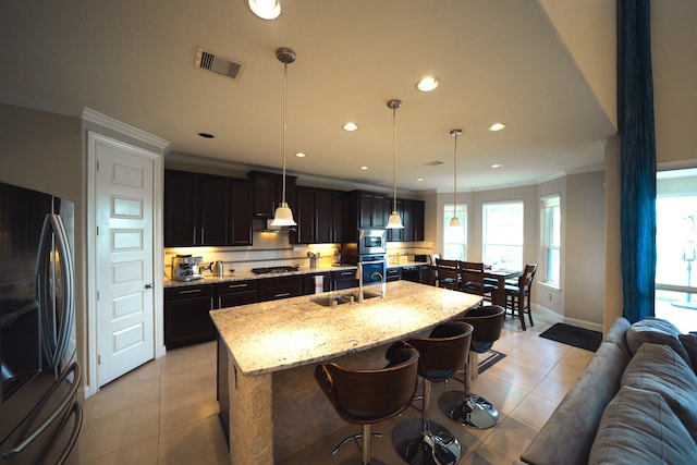 kitchen featuring light stone countertops, stainless steel appliances, sink, decorative light fixtures, and a center island with sink