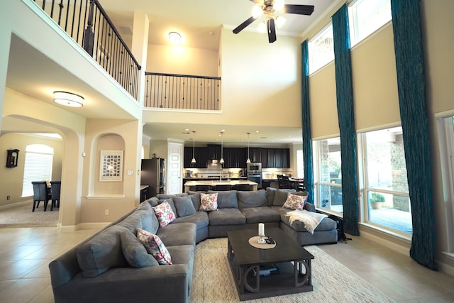 living room with a high ceiling, light tile patterned floors, ceiling fan, and ornamental molding