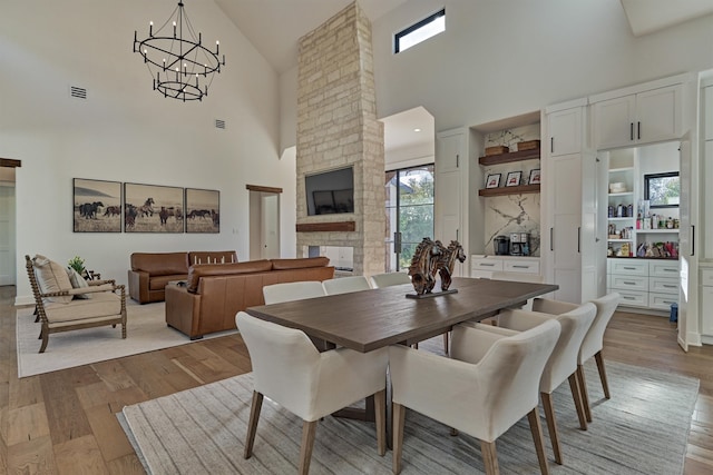 dining room featuring high vaulted ceiling, light hardwood / wood-style flooring, and a stone fireplace