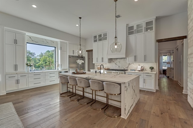 kitchen with built in fridge, light hardwood / wood-style flooring, light stone countertops, an island with sink, and white cabinetry