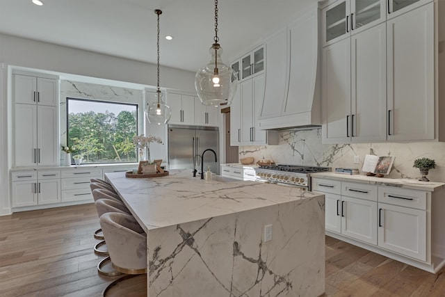 kitchen with light stone countertops, sink, light hardwood / wood-style flooring, an island with sink, and high end appliances